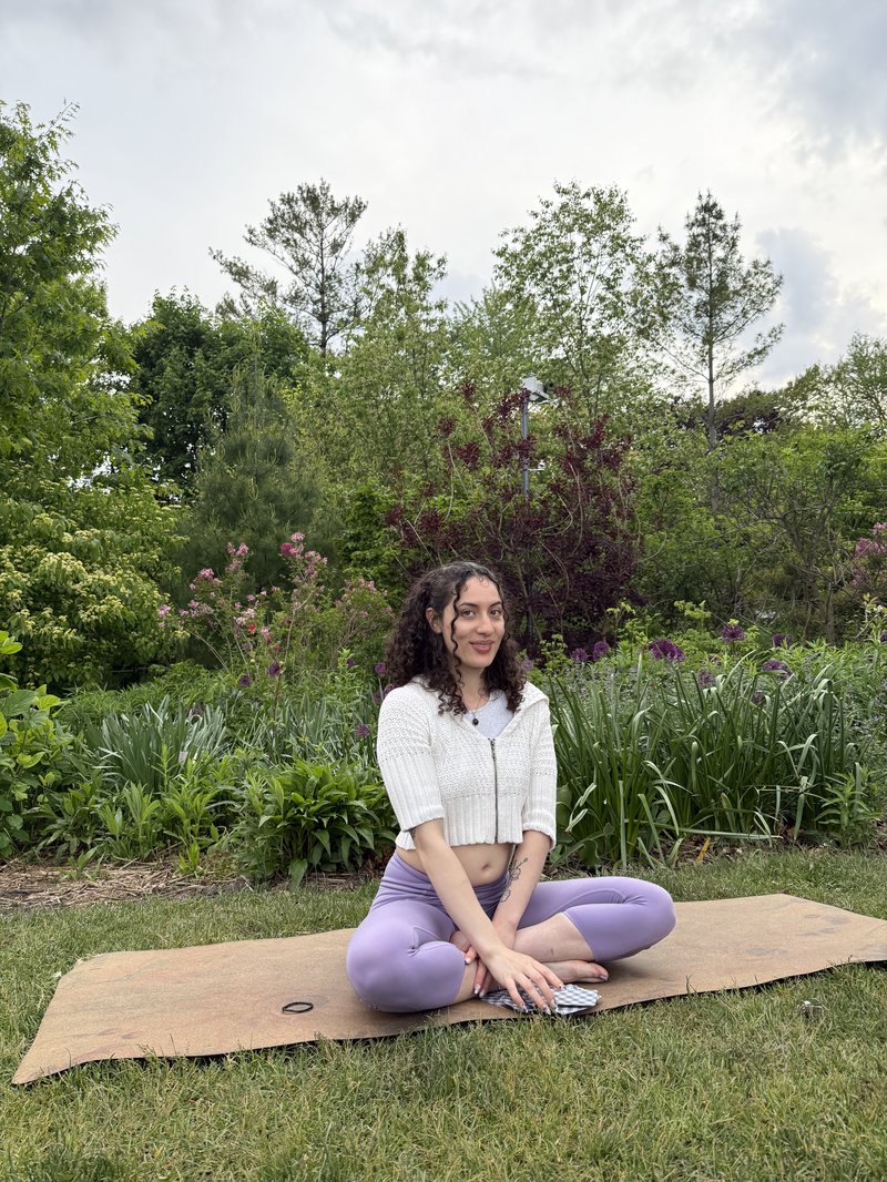 Alli Guzman seated cross-legged on a yoga mat in a garden, smiling