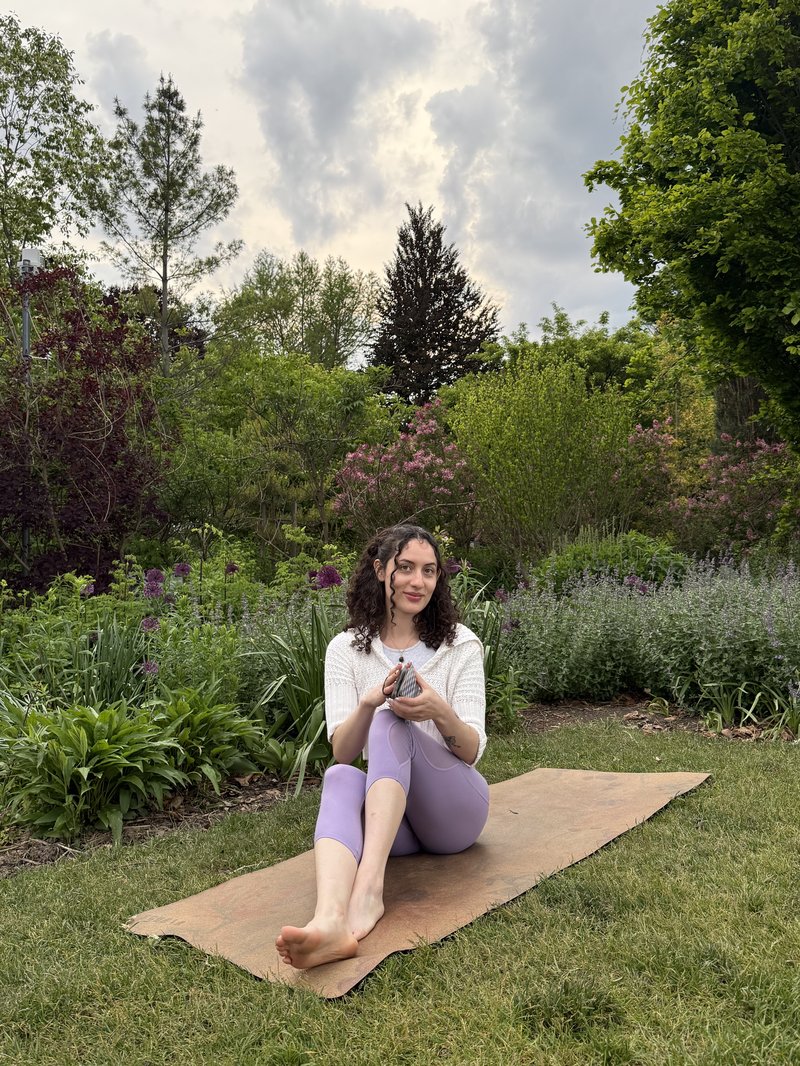 Alli seated on a yoga mat in a garden