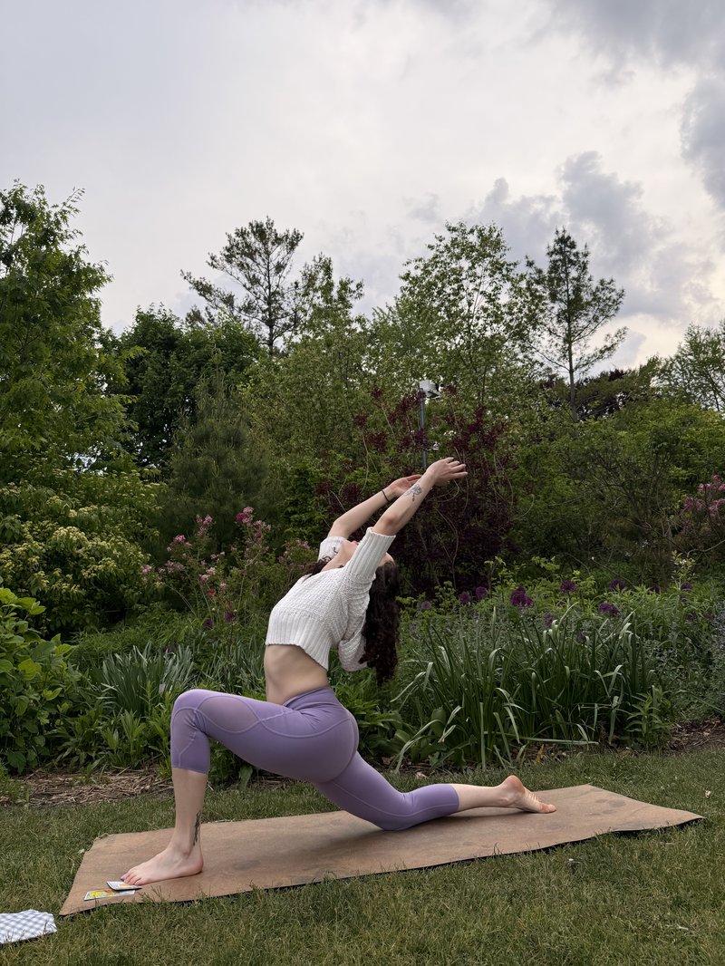 Alli in a deep crescent lunge reaching skyward in a lush garden