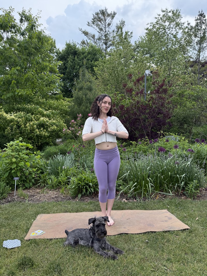 Alli Guzman standing in prayer pose outdoors with her dog at her feet